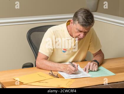 Leitender kaukasischer Mann saß am Schreibtisch zu Hause und vervollständigt das Briefwahl oder Wahlabweser für die Präsidentschaftswahl 2020 Stockfoto