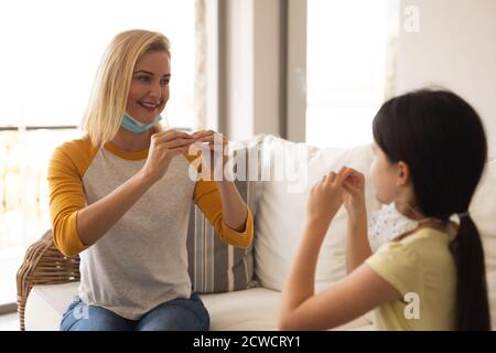 Kaukasische Frau und ihre Tochter verbringen Zeit zu Hause zusammen, tragen Gesichtsmasken, ein Gespräch mit Gebärdensprache. Soziale Distancing duri Stockfoto