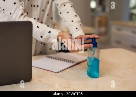 Kaukasische Frau, die von zu Hause aus arbeitet und ihre Hände desinfiziert. Soziale Distanzierung während Covid 19 Coronavirus Quarantänesperre. Stockfoto