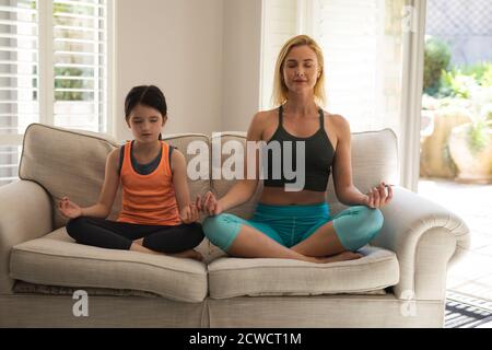 Kaukasische Frau und ihre Tochter verbringen Zeit zu Hause zusammen, Yoga zu tun, meditieren. Soziale Distanzierung während Covid 19 Coronavirus-Quarantänesperre Stockfoto