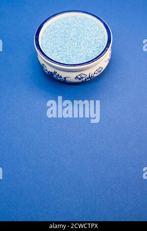 Vertikale Aufnahme von blauem Sand in einer porzellanschale auf Eine blaue Oberfläche Stockfoto