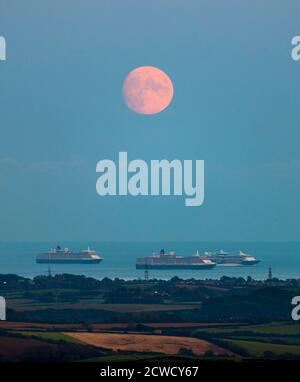 Abbotsbury, Dorset, Großbritannien. September 2020. Wetter in Großbritannien. Blick von Abbotsbury in Dorset auf den fast Vollmond, der über drei der leeren Kreuzfahrtschiffe in Weymouth Bay in den Himmel aufsteigt. Die Schiffe sind Cunards Queen Elizabeth, Queen Victoria und TUI's Marella Discovery. Dieser Mond, wenn er am 1. Oktober voll ist, wird der Erntemond genannt. Bild: Graham Hunt/Alamy Live News Stockfoto