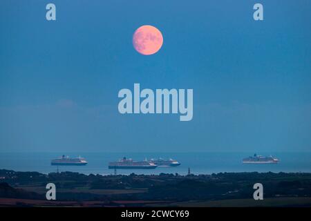 Abbotsbury, Dorset, Großbritannien. September 2020. Wetter in Großbritannien. Blick von Abbotsbury in Dorset auf den fast Vollmond, der über drei der leeren Kreuzfahrtschiffe in Weymouth Bay in den Himmel aufsteigt. Die Schiffe sind Cunard's Queen Elizabeth, Queen Victoria TUI's Marella Discovery und P&O's Arcadia. Dieser Mond, wenn er am 1. Oktober voll ist, wird der Erntemond genannt. Bild: Graham Hunt/Alamy Live News Stockfoto