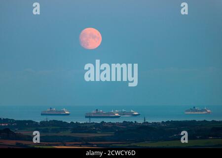 Abbotsbury, Dorset, Großbritannien. September 2020. Wetter in Großbritannien. Blick von Abbotsbury in Dorset auf den fast Vollmond, der über drei der leeren Kreuzfahrtschiffe in Weymouth Bay in den Himmel aufsteigt. Die Schiffe sind Cunard's Queen Elizabeth, Queen Victoria TUI's Marella Discovery und P&O's Arcadia. Dieser Mond, wenn er am 1. Oktober voll ist, wird der Erntemond genannt. Bild: Graham Hunt/Alamy Live News Stockfoto