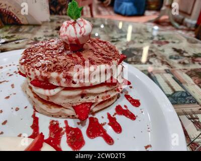 Nahaufnahme von Dessert in einem schicken Restaurant serviert Erdbeer- und Vanillepfannkuchen oben mit einer Eisportionierer Stockfoto