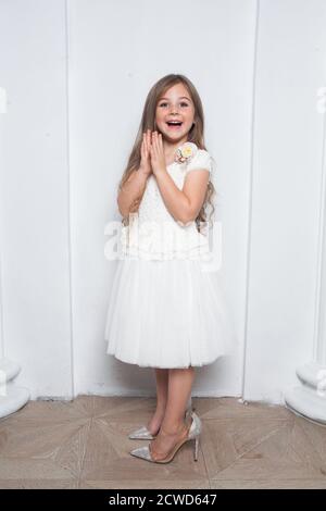 Kleine Prinzessin - aufgeregt emotionale niedliche Mädchen in Mode weiß Kleid mit Spaß und tragen große Mütter funkeln High Heels Schuhe auf weißem Hintergrund Stockfoto