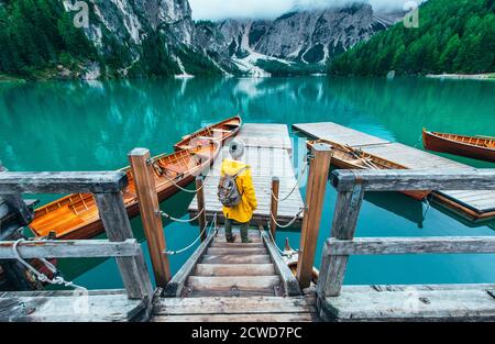 Berggeschichten. Glücklicher Backpacker auf einem Wanderlust Urlaub. Mann mit einem gelben Regenmantel, der vor dem See steht und die Aussicht genießt Stockfoto