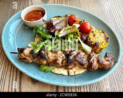 Portion Schweinefleisch Kebab Fleisch auf Holzspieß mit gegrilltem Gemüse auf dem Restauranttisch Stockfoto