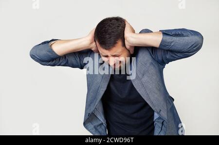 Junger Geschäftsmann mit Bart in einer Jacke. Hände auf dem Kopf, leiden unter Kopfschmerzen in Verzweiflung und unter Stress durch Schmerzen und Migräne. Porträt eines Mannes auf grauem Hintergrund. Stockfoto