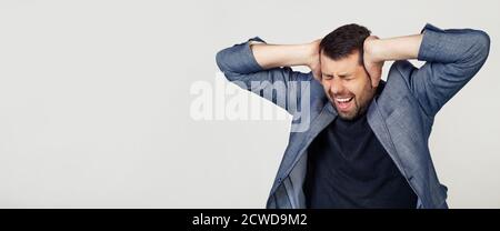 Junger Geschäftsmann mit Bart in einer Jacke. Hände auf dem Kopf, leiden unter Kopfschmerzen in Verzweiflung und unter Stress durch Schmerzen und Migräne. Porträt eines Mannes auf grauem Hintergrund. Stockfoto