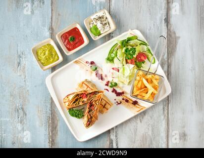 Türkische tantuni in weißem Teller auf Holztisch, serviert mit verschiedenen Saucen und Chips. Stockfoto