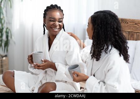 Zwei junge Frauen in Bademänteln sitzen auf dem Bett und trinken Kaffee Stockfoto