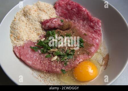 Blick von oben auf einen Teller, in dem Hackfleisch, Ei, Paniermehl, Petersilie und Pinienkerne zu hausgemachten Fleischbällchen gemischt werden Stockfoto