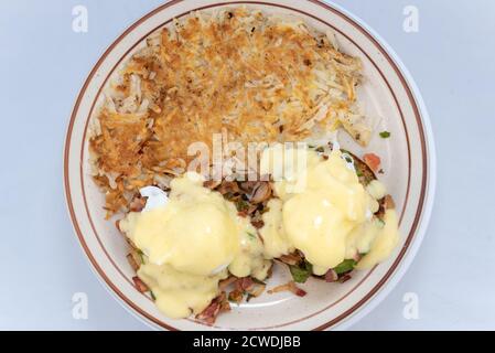 Blick von oben auf die großzügige Serviermahlzeit eines herzhaften Eier benedict hoch gestapelt mit Belag und tropfend mit geschmolzenem Käse. Stockfoto