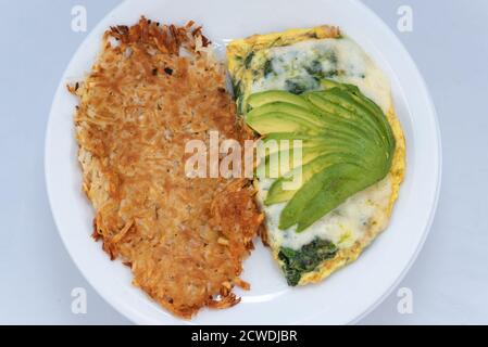 Blick von oben auf eine großzügige Mahlzeit mit einem herzhaften Avocado-Omelett mit Soße kombiniert mit Rösti. Stockfoto