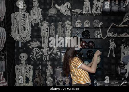 Frau in Pandemie Coronavirus COVID-19 Maske Läden für Halloween Schädel Dekorationen in einem Spirit Halloween Store Stockfoto