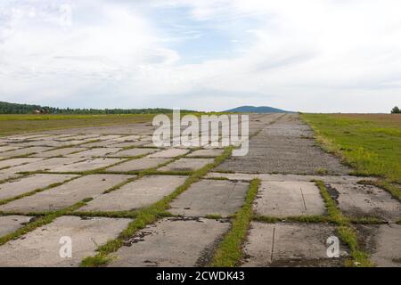 Leerer Betonboden mit grünem Gras unter blauem Himmel, perspektivischer Blick auf den Berg. Stockfoto