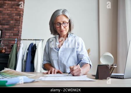 Lächelnd reife stilvolle Frau Modedesignerin Zeichnung Skizzen im modernen Studio. Stockfoto