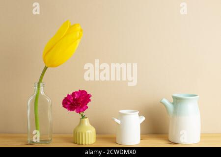 Gelbe Tulpe und rosa Nelkenblume in Vase auf Holztisch mit beigem Hintergrund. Blumenarrangement, Kopierraum Stockfoto