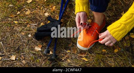 Sportliche Wanderfrau, die nach dem Wandern im Herbstwald Schnürsenkel auf ihre Joggingschuhe schnürt. Wanderkonzept, Outdoor-Lifestyle. Stockfoto