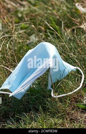 Eine gebrauchte Einweg-blaue Gesichtsmaske achtlos auf Gras entsorgt, während der Covid-19 Pandemie Stockfoto