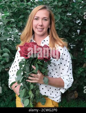 Junge schöne Lehrerin mit roten Rosen. Zurück zur Schule Konzept. Geschenk von Schülern. Lehrer zu Beginn eines Schuljahres. Glücklicher Lehrer mit Blumen. Stockfoto