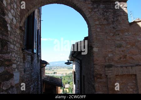 Panoramablick auf die Landschaft Umbriens und einige mittelalterliche Häuser und Ein Bogen im Vordergrund im Dorf Spello Stockfoto