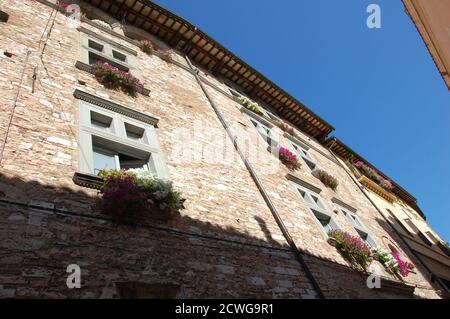 Blick auf ein mittelalterliches Haus und Blumen an den Fenstern Im Dorf Spello in Umbrien und klaren Sommer Himmel oben Stockfoto