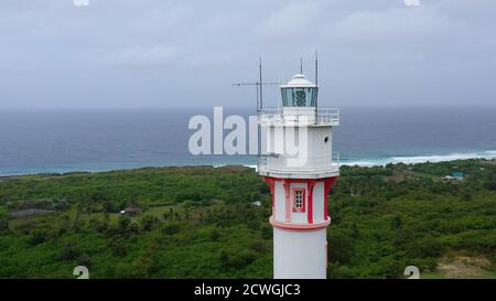 Weißer Turm Leuchtturm auf einer großen Insel, Draufsicht. Regenwaldhügel und Leuchtturmturm. Leuchtturm Bolinao, Luzon, Philippinen. Sommer- und Urlaubskonzept. Stockfoto