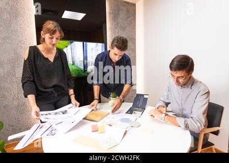 Drei junge Architekten diskutieren gemeinsam in einem Konferenzraum das neue Interior Design Konzept für eine Markenpräsentation. Junge Unternehmer arbeiten Stockfoto