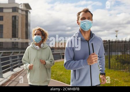 Junge gesunde Paar in Schutzmasken Joggen zusammen in der Morgen in der Stadt Stockfoto