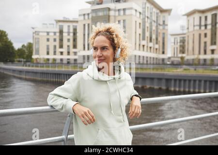 Junge Frau in Kopfhörer stehend auf der Brücke in der Stadt und genießen Sie die Musik Stockfoto