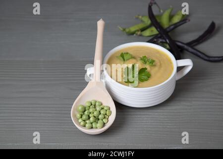 Suppenpürierte Erbsen und Bohnen in einem weißen Becher auf einem grauen Holzhintergrund liegt daneben ein Holzlöffel mit Erbsen. Platz für einen Kopierbereich Stockfoto