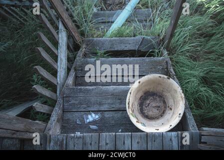Alte hölzerne Veranda eines verlassenen Hauses, schmutziges emailliertes Waschbecken. Ansicht von oben Stockfoto