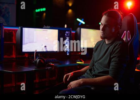 Seriöser junger Mann, der auf einem Stuhl vor Computern sitzt Mit Computerspiel wegschauen er Ruhe nach Spiel Stockfoto