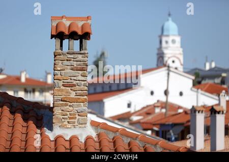 Rote Ziegeldächer mit Steinkaminen vor dem Hintergrund Eine weiße Kirche mit einer blauen Kuppel auf der Insel Von Thassos in Griechenland Stockfoto