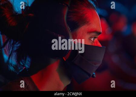 Seitenansicht des jungen Hackers im Kopfhörer und im Schutz Maske mit Computer bei der Arbeit Stockfoto