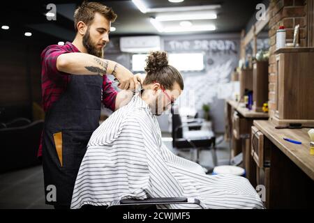 Junger bärtiger Mann, der sich im Friseurladen mit einem elektrischen Rasiermesser von einem Friseur abschneiden lassen kann Stockfoto