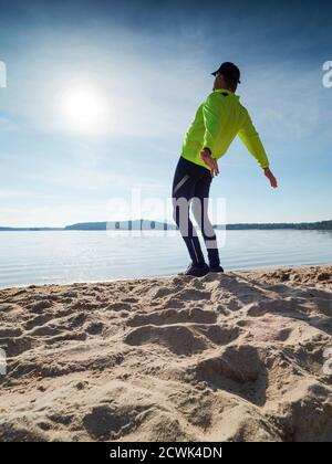 Großer, schlanker Mann, der an einem sonnigen Morgen am Strand Stretching macht. Body Stretching vor dem Sport. Stockfoto