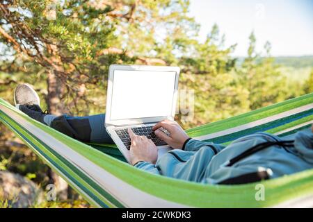 Ein Mann, der an einem Laptop arbeitet, während er in einer Hängematte im Wald liegt. Leerer Bildschirm. Selbstisolierung, Freiberufung, Remote-Arbeit und Distanzierung. Draufsicht Stockfoto