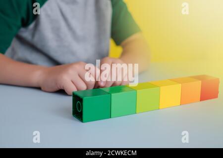 Farbige Blöcke in einer Linie auf dem Tisch. Auf dem Hintergrund der Kinderhände.Konzept der frühen Entwicklung Stockfoto
