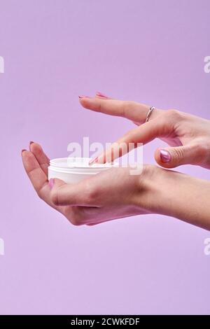 Der Finger der Frau berührt eine Creme im offenen Glas. Stockfoto