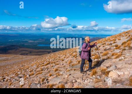 Walker mit Stöcken auf dem Weg zum Berg Cairn Gorm, einem munro in der Nähe von Cairngorm Skigebiet in Aviemore, Schottland, Großbritannien. Loch Morlich im Hintergrund Stockfoto