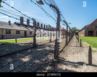 Oświęcim, Polen - Juni 05, 2019: elektrischen Zaun mit Stacheldraht und Ziegel Gefängnis Gebäuden im Konzentrationslager Auschwitz-Birkenau in Oświęcim, Stockfoto