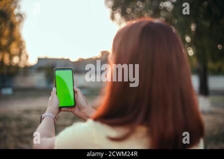 Junges Mädchen mit ihrem Rücken macht Selfie auf einem Smartphone im Park. Leeren Bildschirm auf dem Telefon mockup Stockfoto