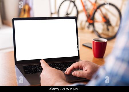 Ein Laptop mit einem leeren weißen Bildschirm auf dem Hintergrund einer häuslichen Umgebung. Der Finger der Hand eines Mannes zeigt auf den Laptop-Bildschirm. Konzept: Remote wo Stockfoto