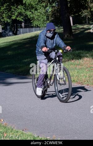 Ein älterer Mann fährt mit seinem Fahrrad und trägt ein Gesicht, das Bandana bedeckt. In einem Park in Flushing, Queens, New York. Stockfoto