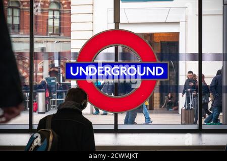 London, Großbritannien - 2. Februar 2020 - London U-Bahn-Schild an der U-Bahn-Station King's Cross St Pancras mit vorbeifahrenden Touristen Stockfoto