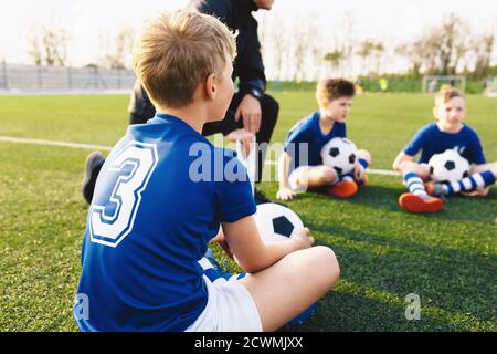 Happy Kids Making Sports on a Grass Venue. Kinder in Blau Fußball Trikot Shirts Zuhören zu Coach Trainingshinweise. Schuljungen üben Sport mit TR Stockfoto