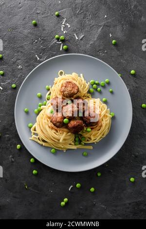 Einfaches Komfort-Essen. Spaghetti mit Fleischbällchen und grünen Erbsen in grauer Platte auf schwarzem Hintergrund Draufsicht Kopierraum Stockfoto